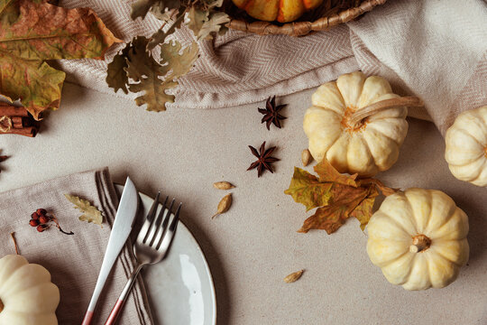 Flatlay with white pumpkins, spices, dry leaves and cutlery on fabric napkin in autumn setting..