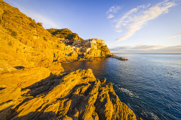 View of golden light kissing the rugged cliffs as the village clings to the hillside, overlooking the vast, serene expanse of the sea, Manarola, Liguria, Italy.