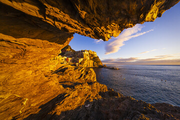 View of golden cliffs and the sea meet under a cave, revealing the vibrant village clinging to the coast in Cinque Terre National Park, Manarola, Liguria, Italy.