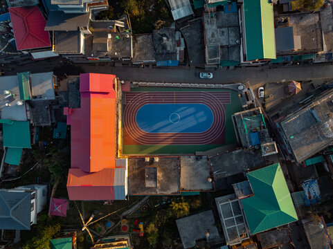 Aerial view of a vibrant sports field nestled among buildings with colorful roofs, creating a striking contrast against the urban landscape, Bir, Himachal Pradesh, India.