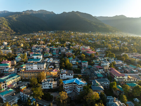 Aerial view of the town nestled between rolling hills, with colorful rooftops and lush greenery bathed in the warm golden light, Bir, Himachal Pradesh, India.