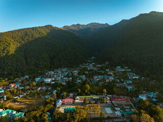 Aerial view of a small town nestled in a valley, overlooked by a mountain range, with buildings exhibiting a variety of colors, Bir, Himachal Pradesh, India.