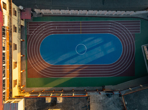 Aerial view of a vibrant running track with concentric lanes and a blue center, surrounded by buildings, Bir, Himachal Pradesh, India.