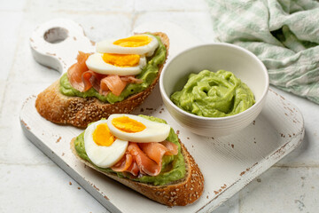 White  board with two Smoked Salmon toast with creamy Avocado. Sesame seeds bread, boiled egg. Close up of homemade open sandwich. Healthy breakfgast.