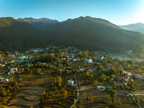 Aerial view of a serene valley nestled between verdant mountains, with scattered buildings and winding paths catching the warm sunlight, Bir, Himachal Pradesh, India.