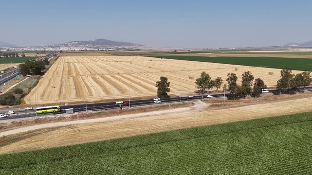 Aerial view of an agricultural valley with harvested fields, green crops, a road, and distant mountains under a clear sky