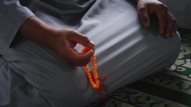 Close-up of hands reciting dhikr using prayer beads against a blurred background. Hands reciting dhikr. A man reciting dhikr while holding a prayer beads. A Muslim's worship activity.