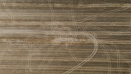 Abstract top-down aerial view of a harvested field showing complex patterns of tire tracks overlaid on the linear stubble