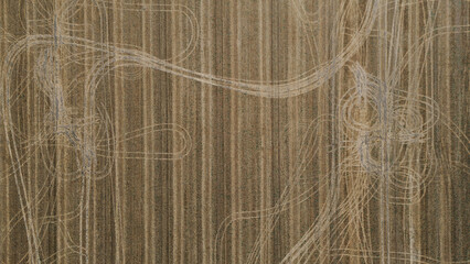 Abstract top-down aerial view of a harvested field showing complex patterns of tire tracks overlaid on the linear stubble