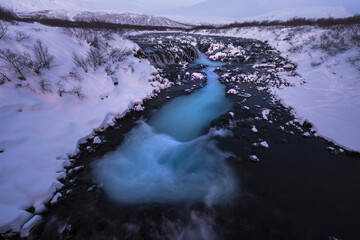 View of the Brúarárfoss waterfall's turquoise waters contrasting against the snow-covered landscape, a serene winter scene, Hlauptunga, Blaskogabyggd, Iceland.