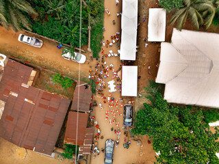 Aerial view of a vibrant gathering along a dusty road lined with buildings and lush trees, Orlu, Imo State, Nigeria.