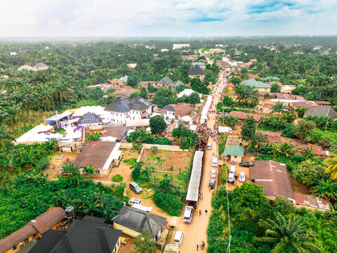 Aerial view of a bustling street flanked by lush greenery and buildings with corrugated iron and dark roofs, a vibrant contrast of nature and buildings, Owerri, Imo State, Nigeria.