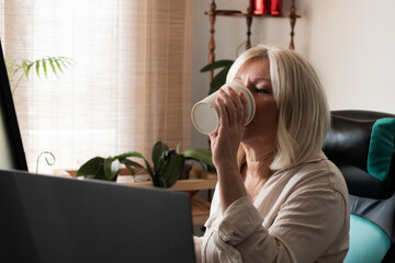 Senior woman working on laptop drinking coffee at home