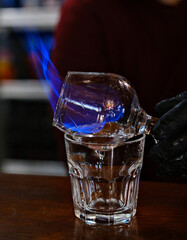close-up of crystal goblet with delicious red alcoholic cocktail that two men bartenders impressively sets to fire at dark bar. Bartender makes hot cocktail.