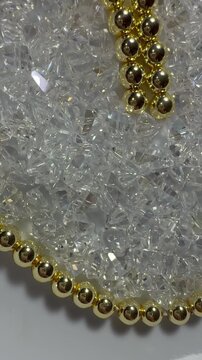 A heart made of polished golden hematite beads with shimmering triangular glass beads inside. Sparkling, jewelry-grade materials perfect for craft, design, and holiday themes