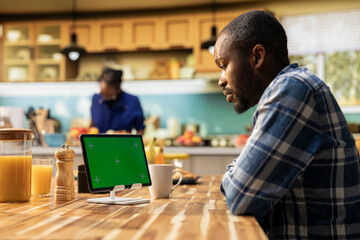 Chroma key tablet on the table where man serves coffee and croissants in a cozy kitchen, boyfriend enjoys relaxed morning routine with symbolizing healthy habits and weekend relaxation.