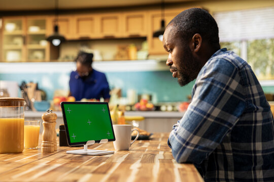 Chroma key tablet on the table where man serves coffee and croissants in a cozy kitchen, boyfriend enjoys relaxed morning routine with symbolizing healthy habits and weekend relaxation.