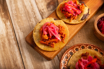 Panuchos, a typical dish from Yucatan, Mexico. A handmade, fried corn tortilla filled with beans, topped with cochinita pibil, pickled red onion, and habanero pepper.