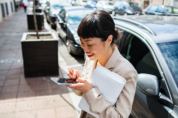 Adult businesswoman smiling while texting on city street
