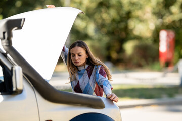 Woman experiencing car trouble, looking at open hood