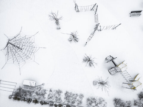 Aerial view of a snow-blanketed playground with intricate climbing frames and bare trees casting subtle shadows on the crisp white surface, Vilnius, Vilnius, Lithuania.