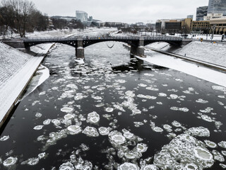 Aerial view of ice floes drift along the Neris River under a bridge, amidst the snowy banks of a winter landscape, Vilnius, Vilnius, Lithuania.