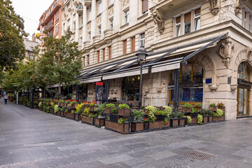 Fototapeta premium Outdoor café terrace with modern furniture, wooden tables, woven chairs, and large awnings