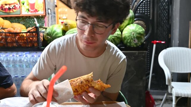 Istanbul, T&uuml;rkiye, August 1, 2025. Portrait of a young Caucasian man biting into a freshly served kebab. He looks into the camera. Local food specialties.