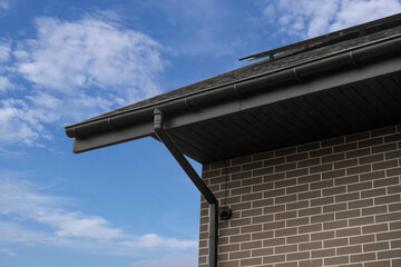 Black rain gutter system on brick house roof corner against sky © Sergey