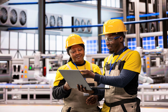 African american engineers at smart manufacturing plant analyzing automated production systems using laptop. Male and female technicians improving digital automation assembly line performance. - Powered by Adobe