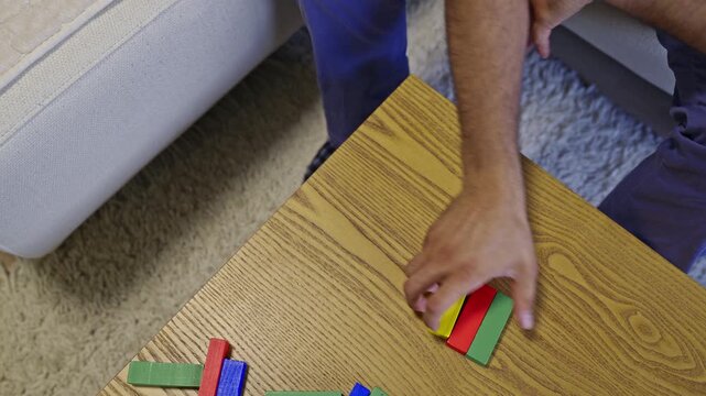 A person is engrossed in building structures with vibrant, colorful wooden blocks on a textured wooden table. The distinct sounds of the blocks clicking and clacking together enhance the experience.