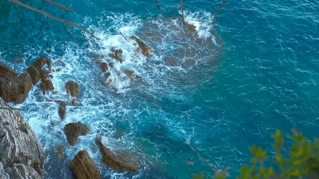 Azure ocean waves crashing on rocky coastline. Breathtaking aerial view of turquoise sea waves breaking on rugged cliffs, revealing the serene and wild beauty of a secluded coastal landscape