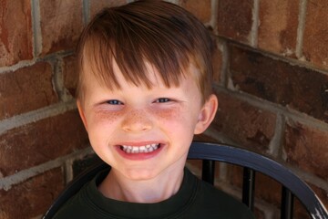 Heartwarming Close-up: Smiling Freckled Boy with Vivid Blue Eyes and Brown Hair Against Brick