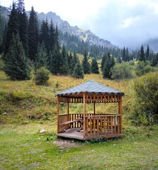 A wooden gazebo against the backdrop of a mountain landscape and pine forest