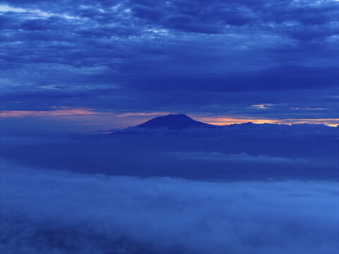Aerial view of Mount Lawu covered in thick, fluffy clouds under the rising sun, Klaten Regency, Central Java, Indonesia.