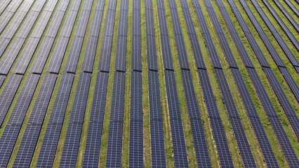 Aerial view of a large solar panel farm with rows of photovoltaic panels and green grass landscape
