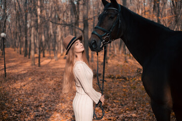 Young woman interacting with a large horse on a scenic autumn path lined with trees