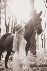 Woman in a white dress and hat stands beside a horse in a sunlit forest during a serene afternoon
