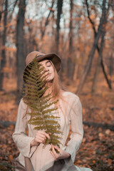 Woman holding a fern in a serene forest during autumn sunset surrounded by fallen leaves