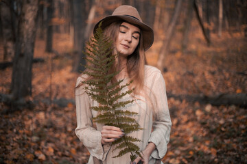 Woman holding a fern in a serene forest during autumn sunset surrounded by fallen leaves