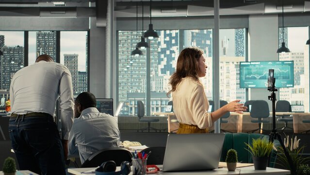 Corporate staff filming a video advertisement for a commercial in office, collaborating on data visualization and report sharing. Work team discusses resource allocation and targets.