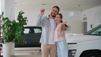 Happy couple showing keys to new car at dealership