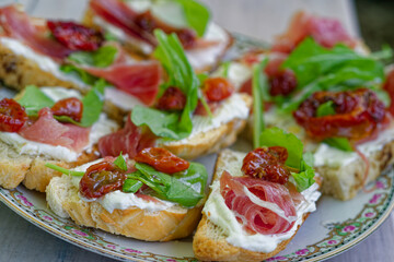 Bruschetta appetizer with prosciutto, ricotta, sun-dried tomatoes, arugula