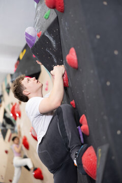 Teenage boy visitor to fitness club clambs wall for amateur climbers, side view. Active recreation, hobbies, recreation for active and sporty people