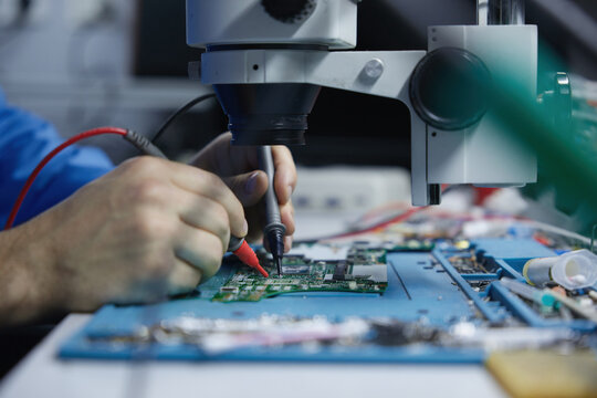 Electronics repair technician working under microscope