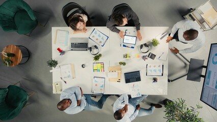 Top down view of conference with investors group discussing performance reports, insights and planning. Professional team evaluates financial data and forecasting for targets.