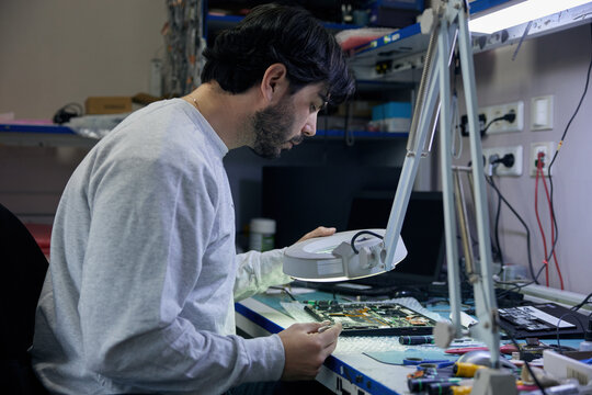 A man is working on a motherboard with a magnifying glass
