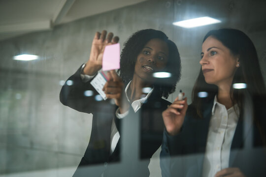 Businesswomen brainstorming ideas using sticky notes on glass wall