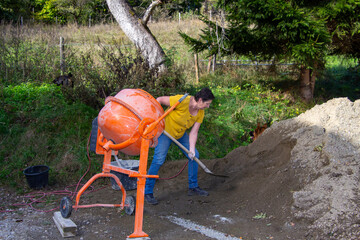 Woman puts cement with a shovel into the cement mixer.