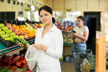 In vegetable department of supermarket,asian woman shopper thoughtfully chooses large fruits of Bulgarian pepper